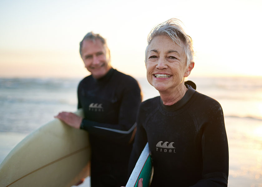 Retired couple holding surf boards on the beach